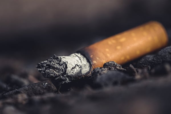 This image depicts the smoldering end of a used cigarette perched on a pile of ashes. It symbolizes the dangers of smoking, which include an increased risk of lung cancer and sometimes mesothelioma. 